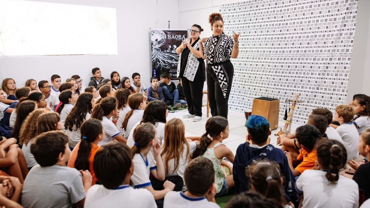 espetáculo em Itajaí,imigração angolana em Itajaí,ancestralidade negra,cultura africana em Itajaí,espetáculo Angola,histórias sobre Angola,escolas de Itajaí,Rede Municipal de Ensino de Itajaí,cultura em Itajaí,teatro em Itajaí,imigração africana em Santa Catarina,comunidade angolana em Itajaí,história da imigração angolana,narrativas africanas,contação de histórias,ancestralidade africana,movimento negro em Itajaí,espetáculos gratuitos em Itajaí,programação cultural Itajaí,apresentações gratuitas nas escolas